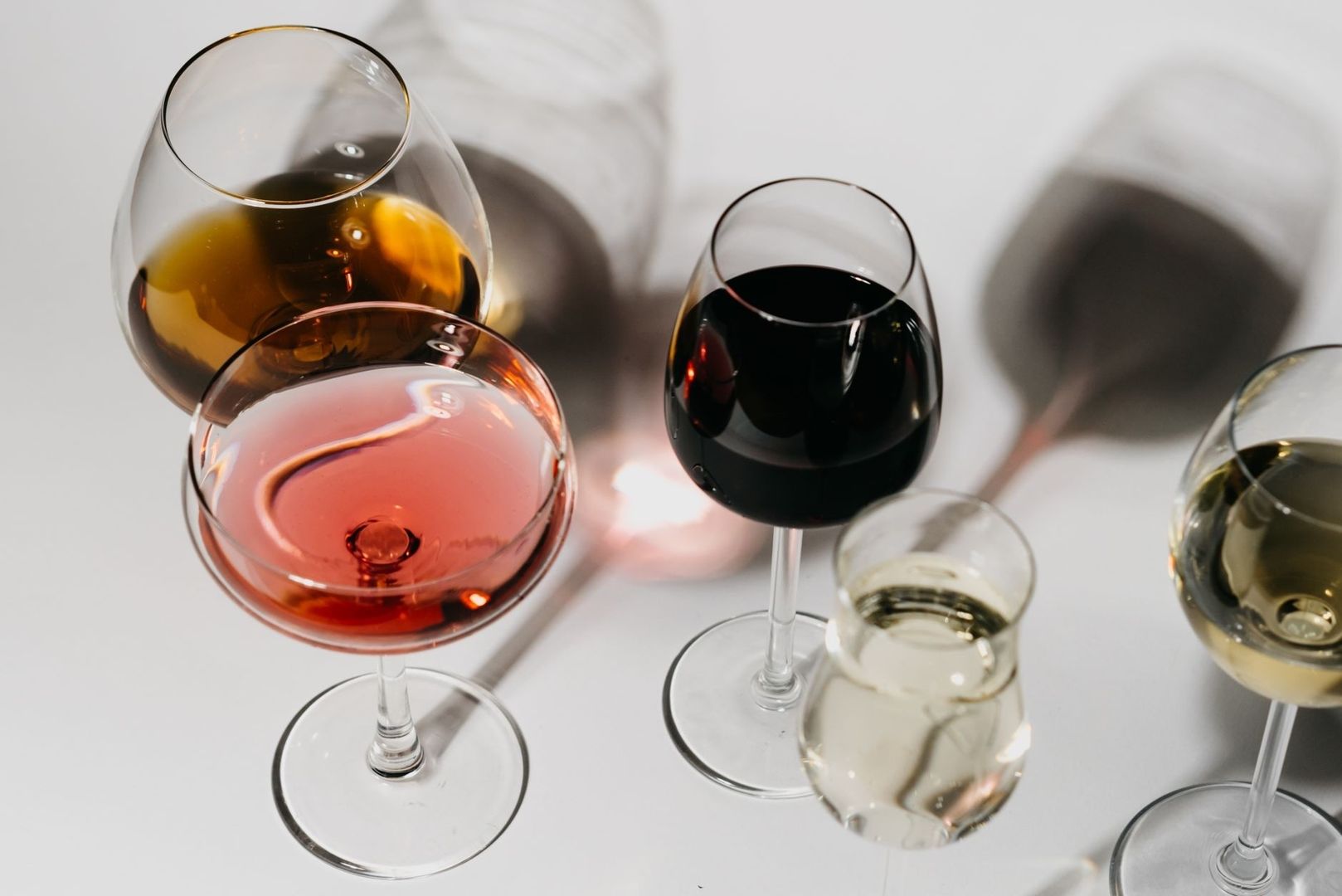 Flere vinglas med rød, rosé, hvid og mørk vin på et lyst bord